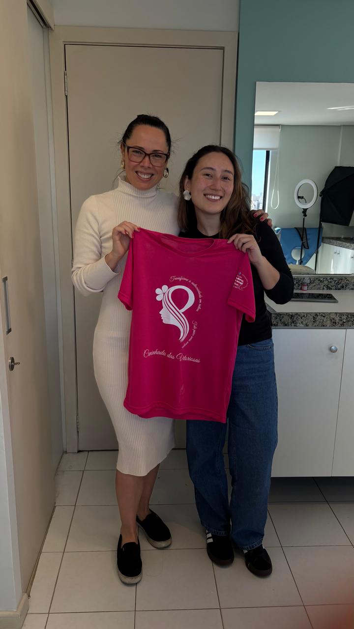 Dra. Fernanda e participante segurando a camiseta rosa na clínica