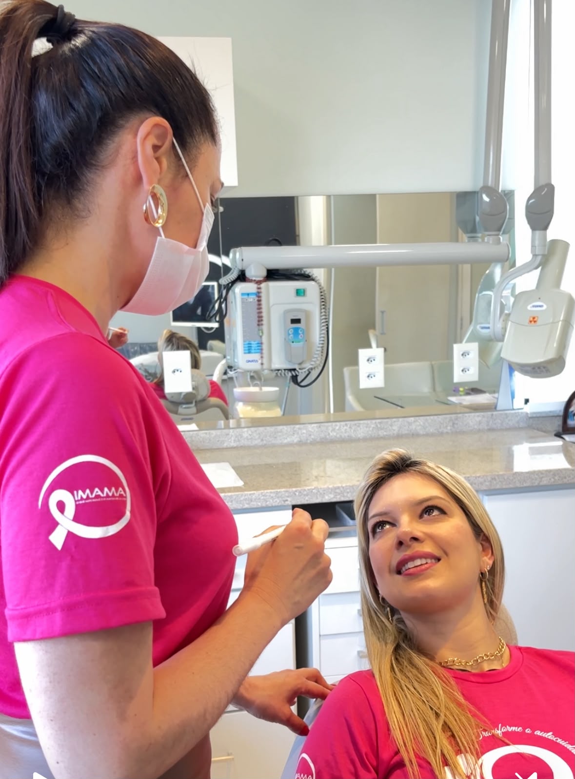 Dra. Fernanda atendendo Vere, ambas com camisetas rosa do IMAMA